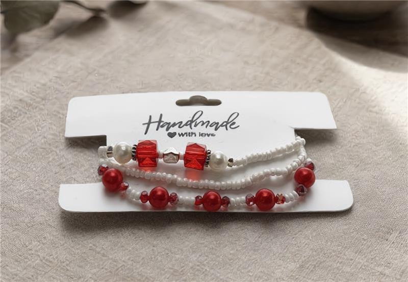 Set of beaded bracelets on a white card with 'Handmade with Love' text, on a beige fabric background.
