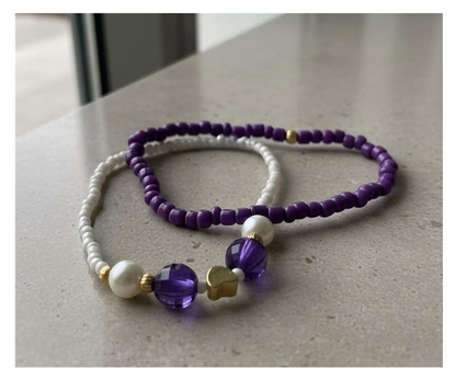 Two beaded necklaces with purple and white beads on a light surface.