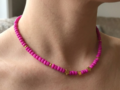 Person wearing a pink beaded necklace with gold accents on a neutral background