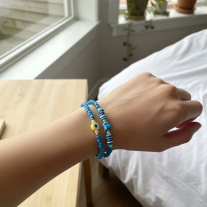 Hand wearing two blue beaded bracelets with a blurred indoor background