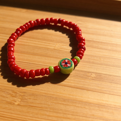 Red beaded bracelet with a floral charm on a wooden surface