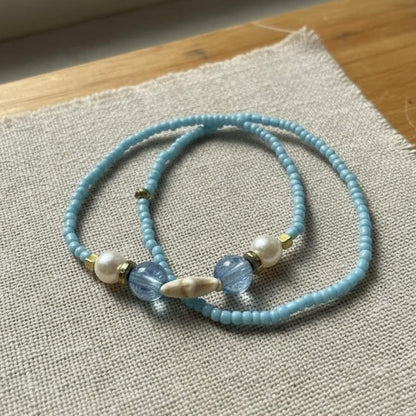 Light blue beaded necklace with pearls on a textured fabric surface