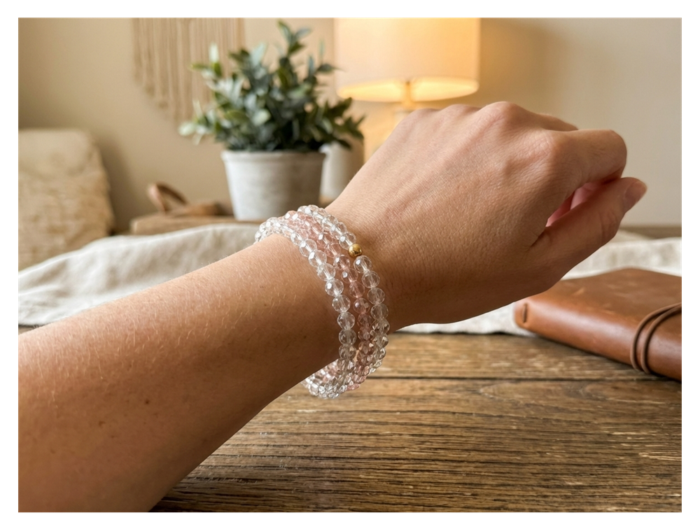 Hand wearing a clear beaded bracelet on a wooden surface with a cozy indoor background