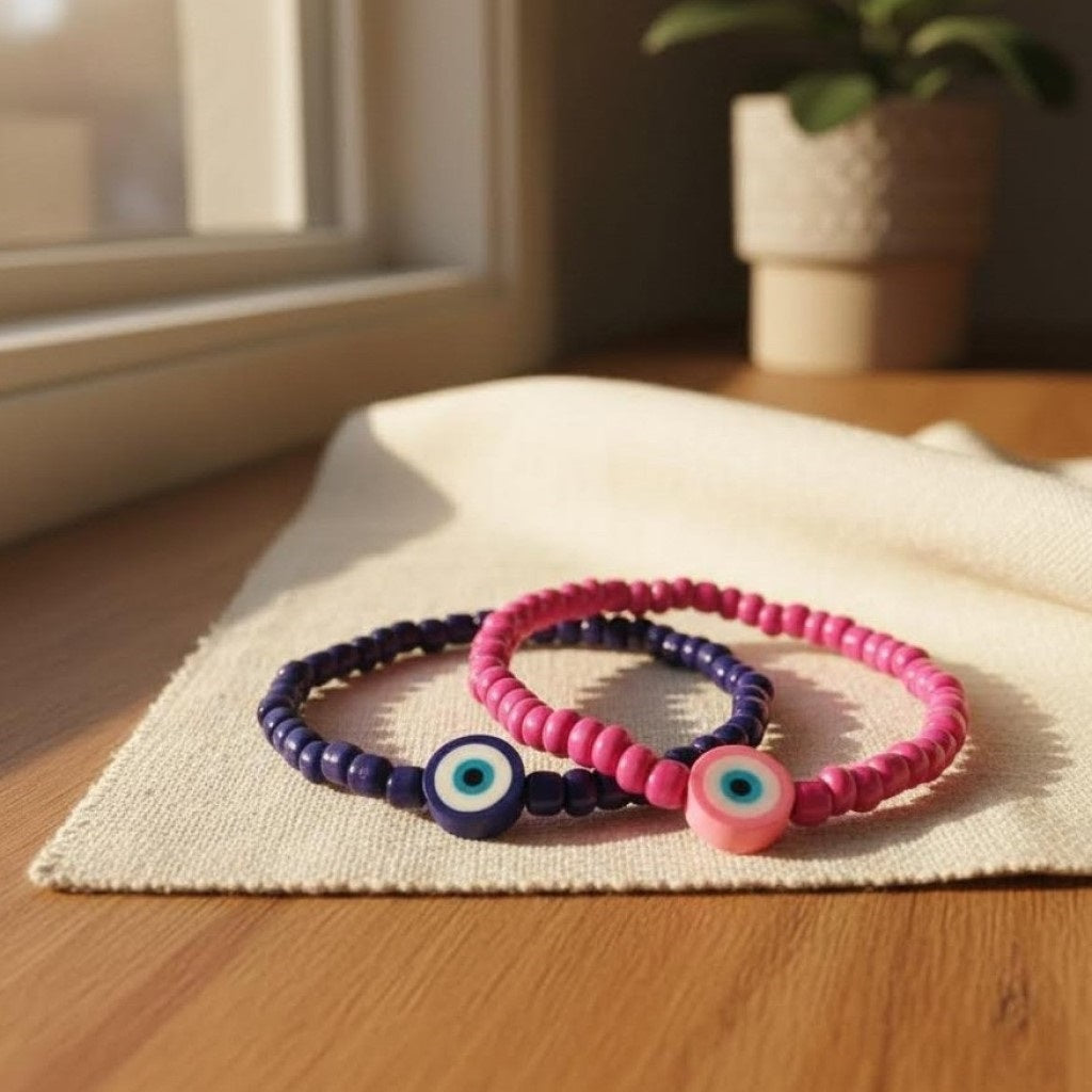 Two beaded bracelets, one pink and one purple, with eye designs on a wooden surface.