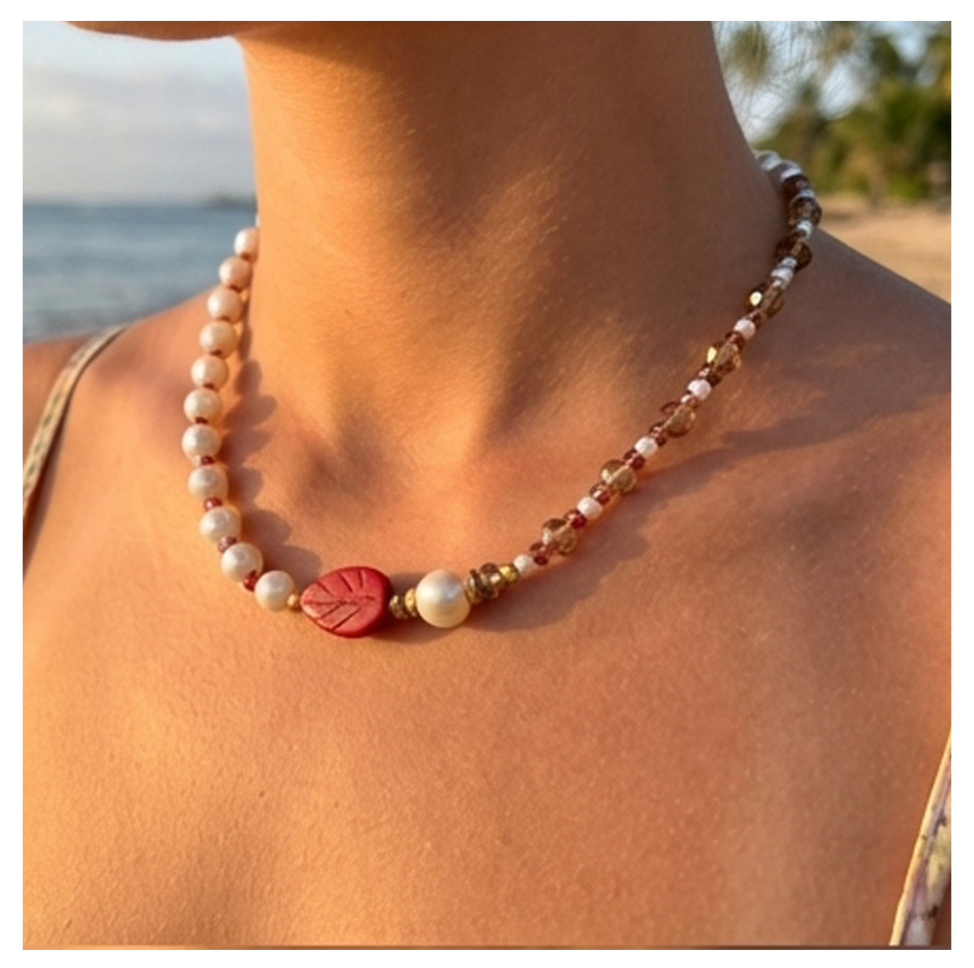 Necklace with a red leaf pendant worn by a person on a beach.
